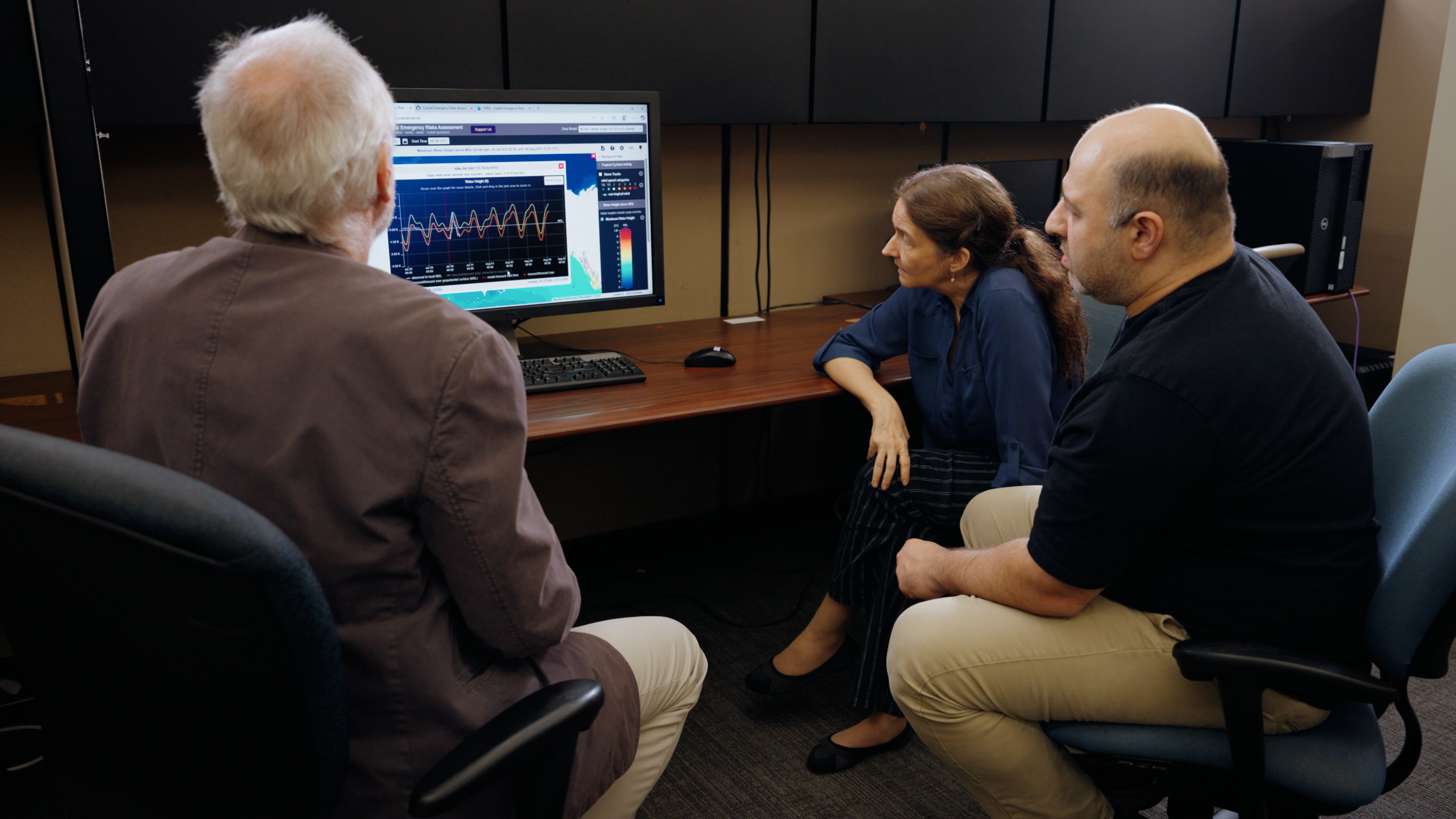 Three researchers gathered around a computer screen displaying the CERA storm surge tool