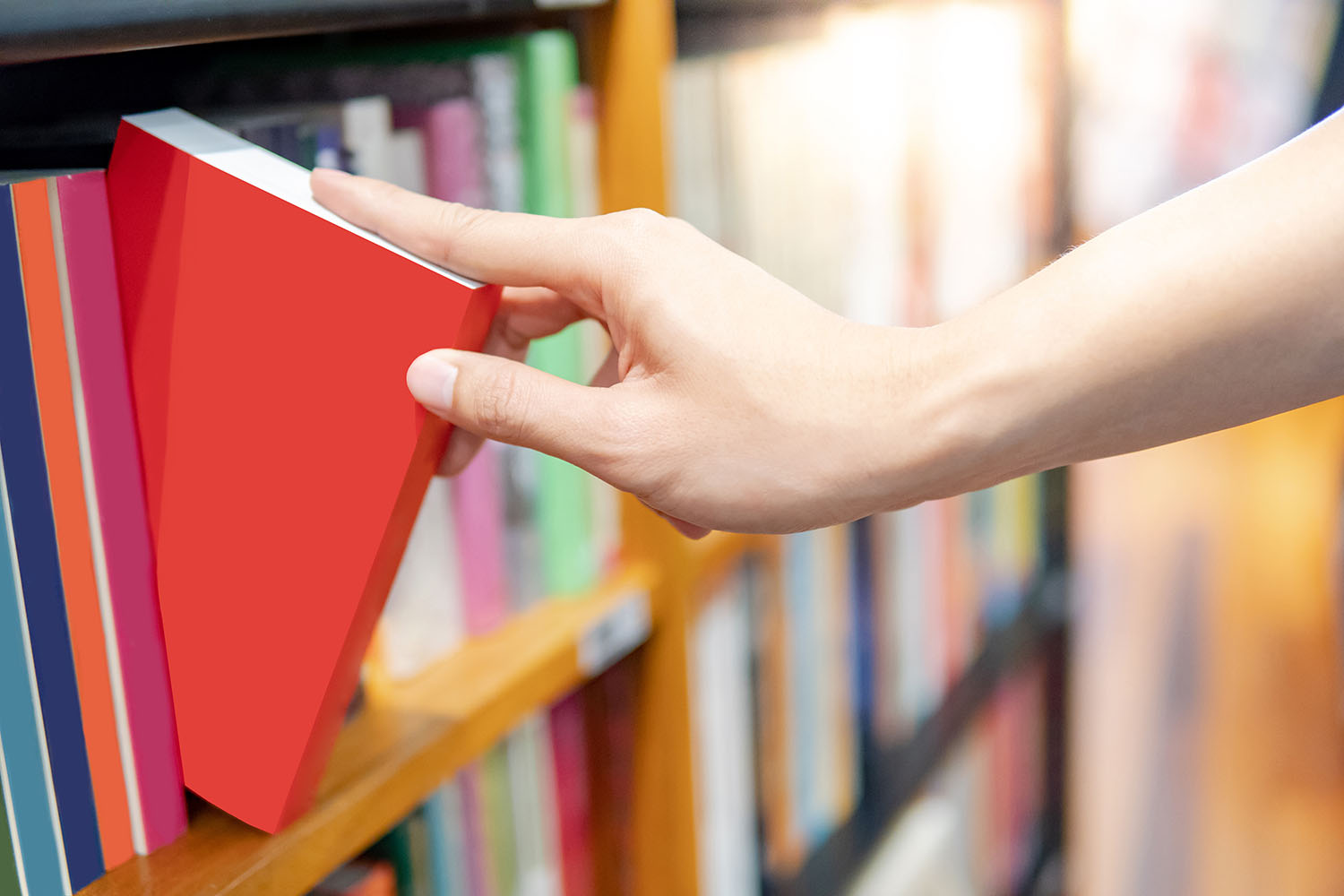 a hadn reaching for a book on a bookshelf