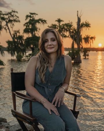 Photo of LSU Honors alum Jordan LaHaye Fontenot sitting in a chair behind the sunset on a swamp.